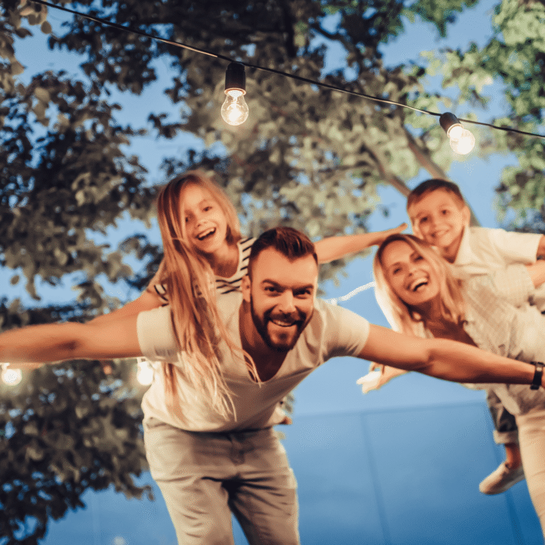 Familia feliz fingiendo volar con los brazos abiertos bajo guirnaldas de luces
