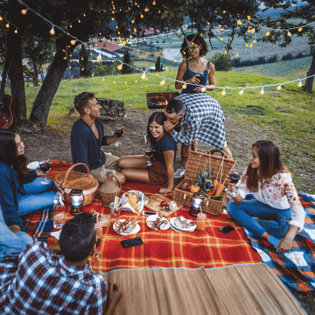 Picnic en grupo sobre la hierba con mantel de cuadros rojos y guirnaldas de luces