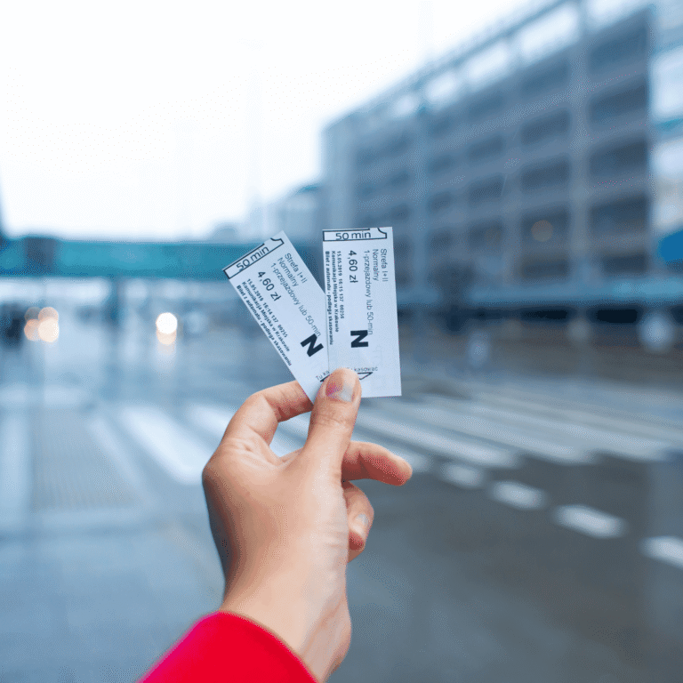 Mano sujetando dos entradas ante un edificio desenfocado: pases y entradas