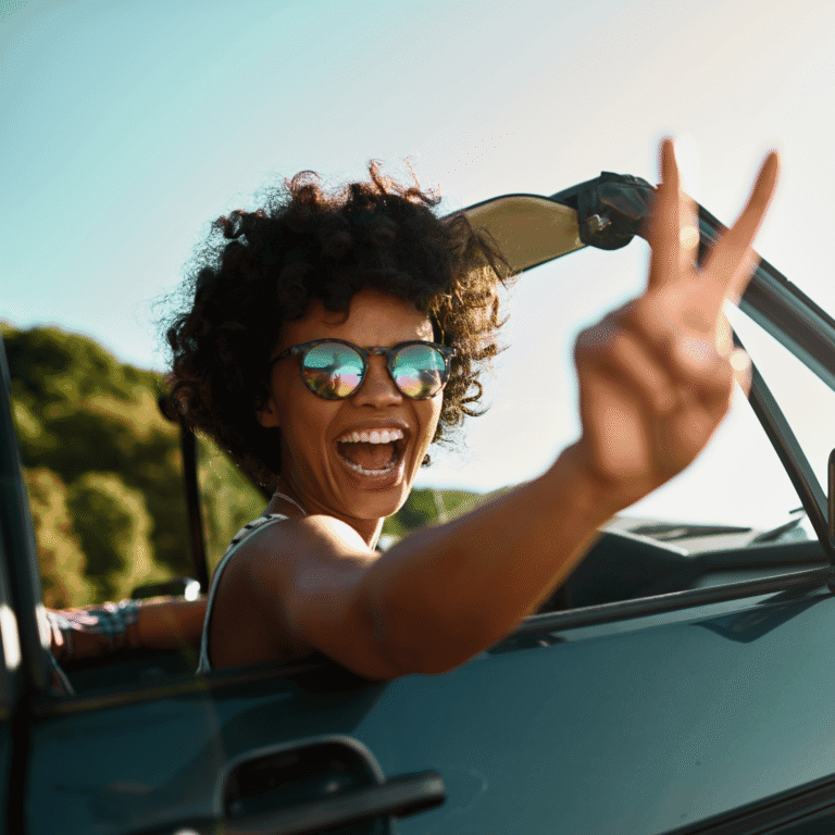 Smiling woman in sunglasses in a convertible making a victory sign: getting there by car